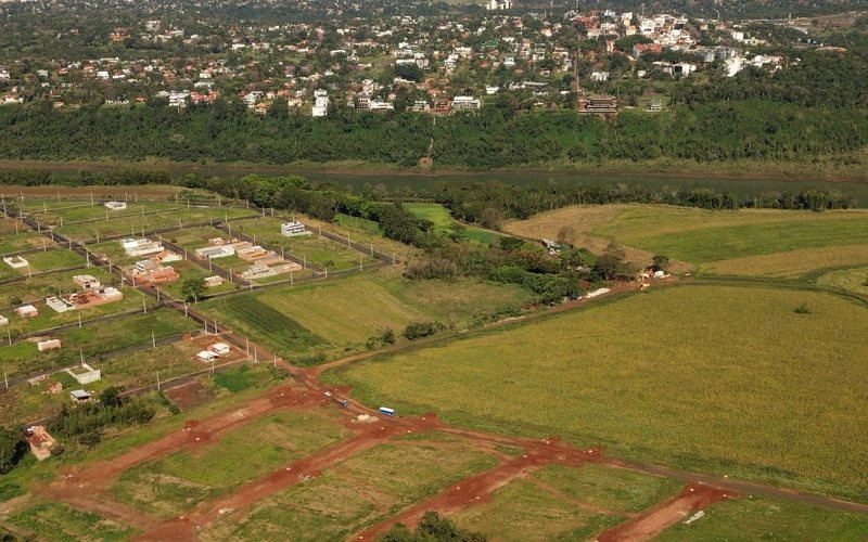 Vista aérea do loteamento ao lado do núcleo já construído, com casas prontas, postes e ruas abertas.